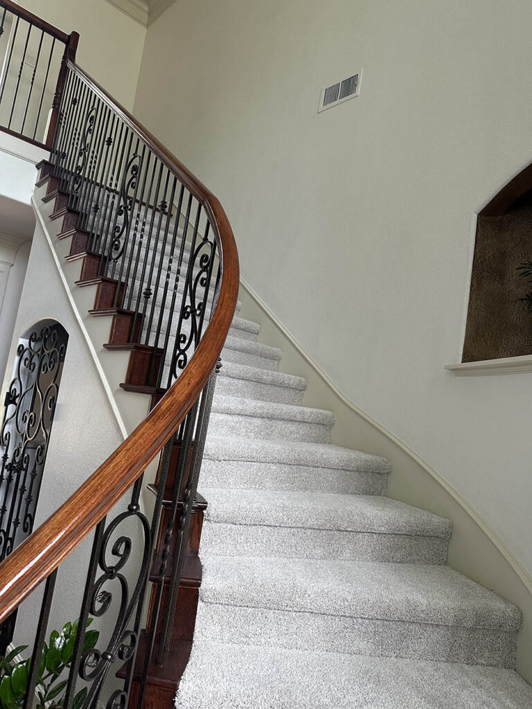 Curved staircase with carpeted stairs and iron railing after a move-out clean