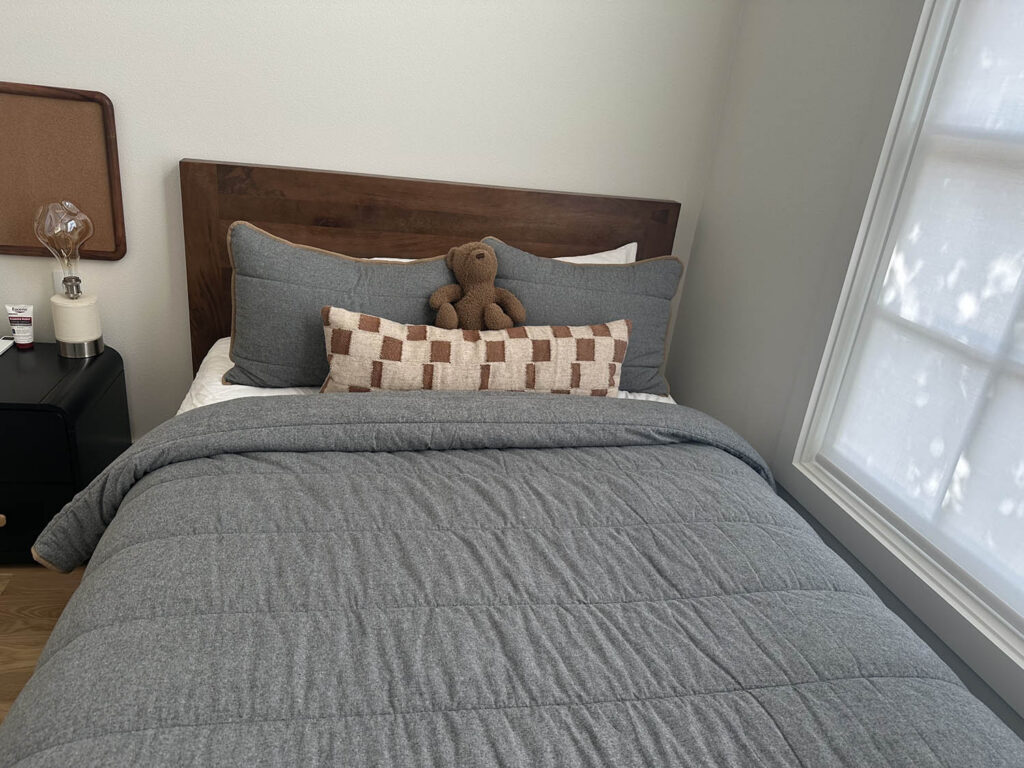 Small bedroom with a made bed and wood headboard after a house cleaning