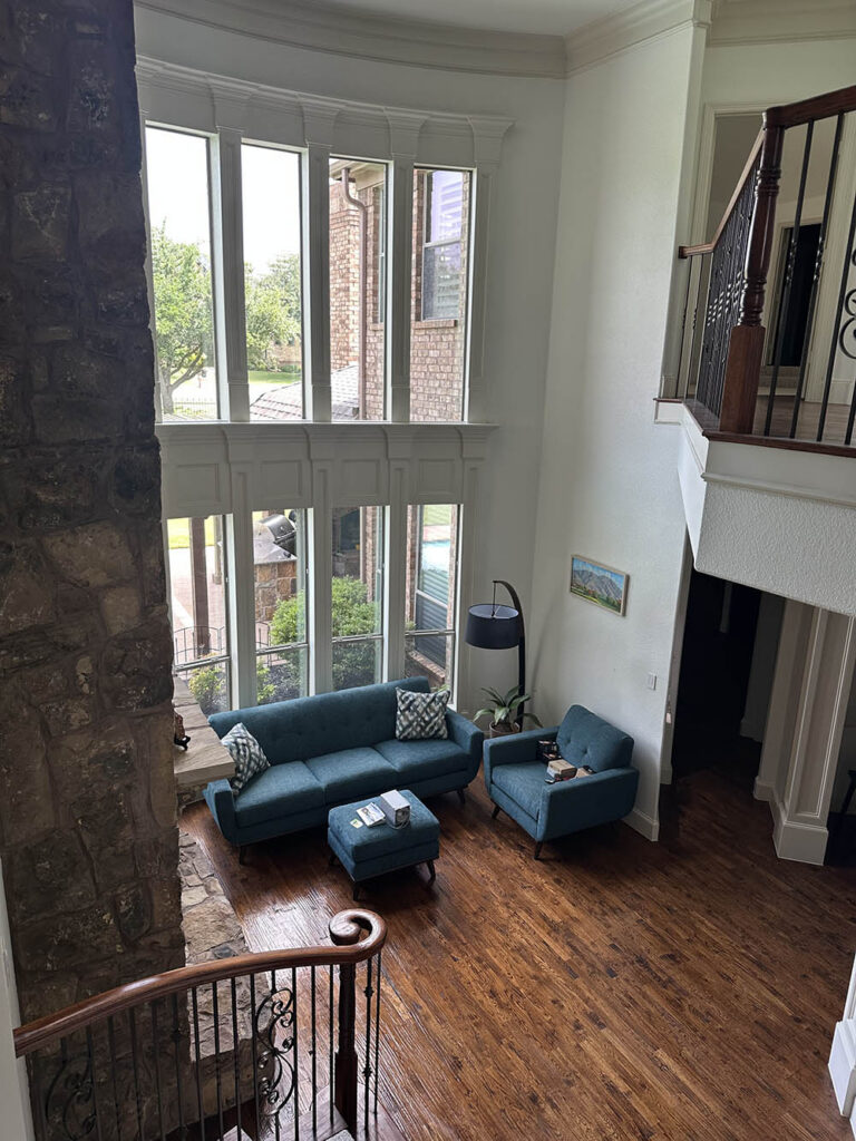 Two-story living room with tall windows and hardwood floors after a house cleaning