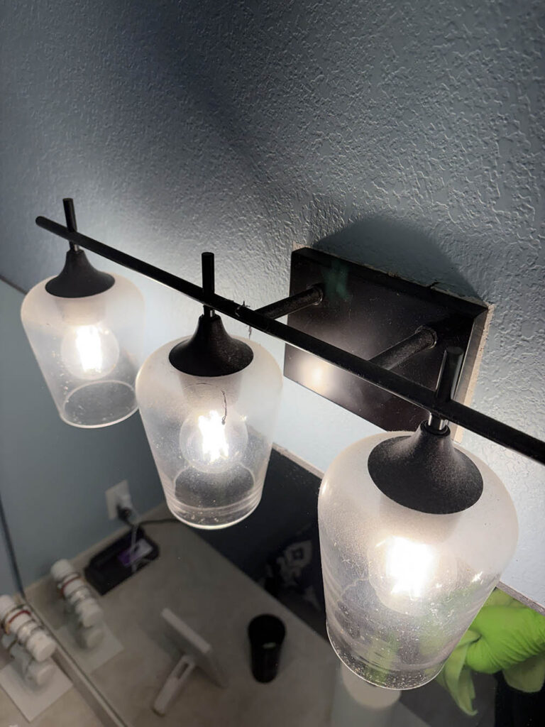 Open Hands crew member in gloves cleaning a bathroom light fixture